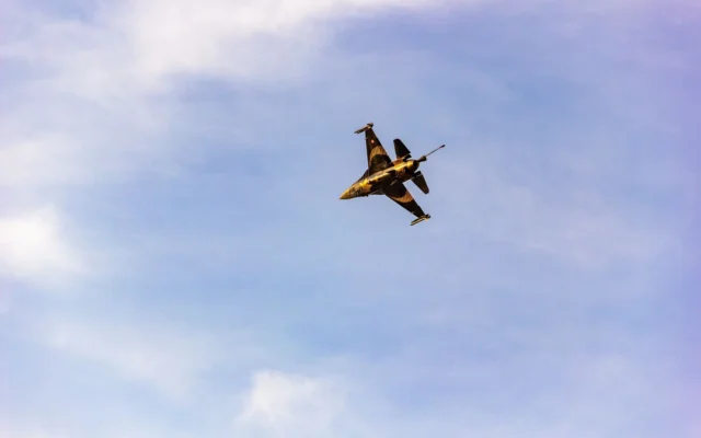 Avion militar cu marcaje galbene și negre, fotografiat de jos în zbor pe cer albastru