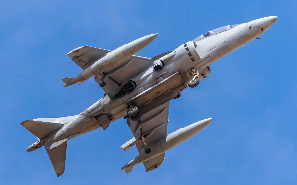 Avion militar fotografiat de jos în zbor pe cer albastru, cu trenul de aterizare coborât