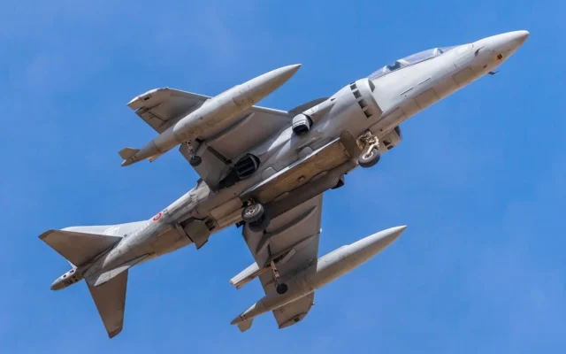 Avion militar fotografiat de jos în zbor pe cer albastru, cu trenul de aterizare coborât