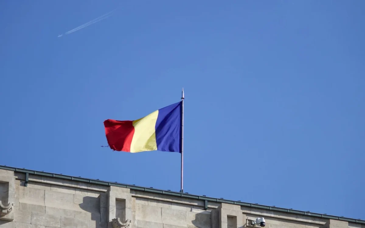 Drapelul României pe un catarg deasupra unei clădiri, pe fundal de cer albastru