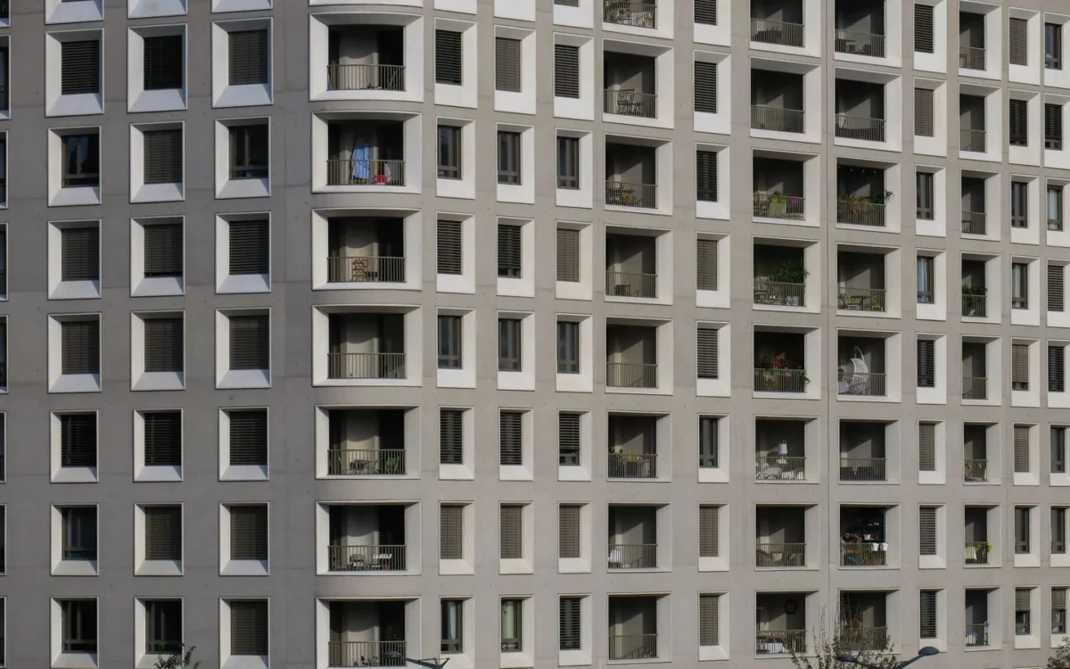 Fațadă gri de bloc de locuințe, cu ferestre și balcoane pe mai multe etaje
