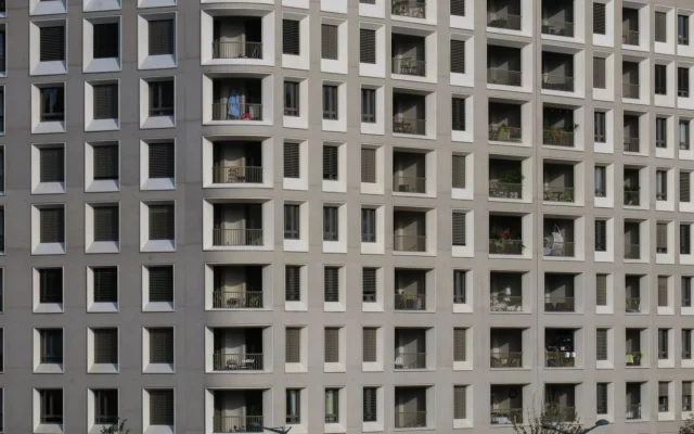 Fațadă gri de bloc de locuințe, cu ferestre și balcoane pe mai multe etaje