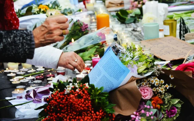 Mâini care aprind lumânări lângă buchete de flori