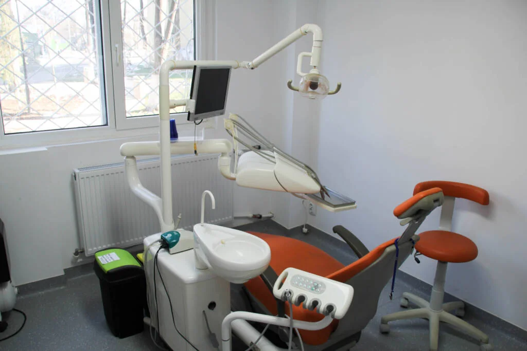 Scaun stomatologic portocaliu și unit dentar lângă fereastră