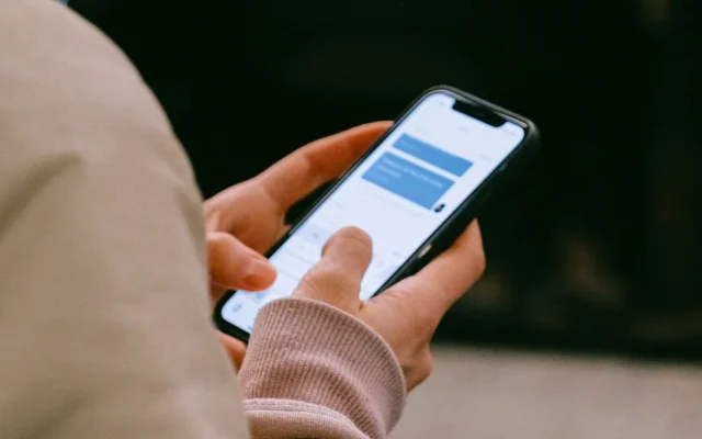 Mâinile unei persoane care folosește un telefon mobil