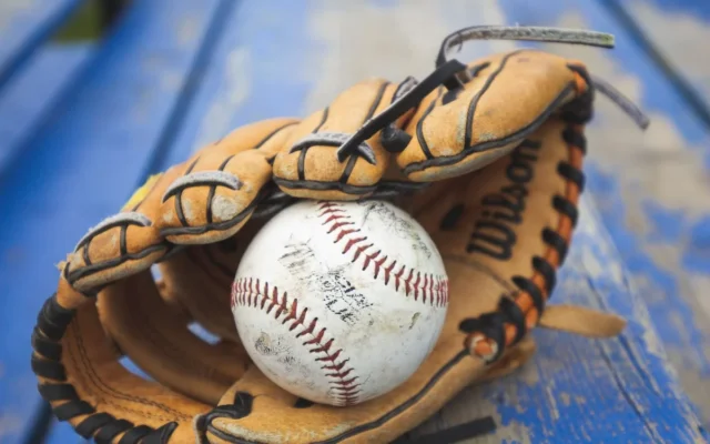 Minge albă de baseball într-o mănușă maro, așezată pe o bancă albastră
