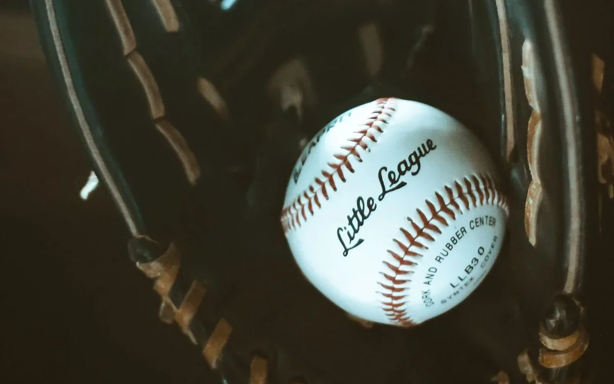 Minge albă de baseball cu cusături roșii într-o mănușă din piele maro