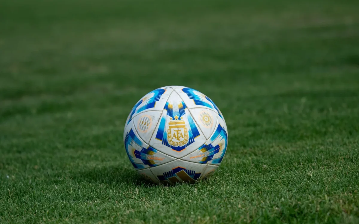 Minge de fotbal albă cu modele albastre și aurii pe iarbă verde