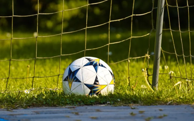 Minge de fotbal albă cu model negru, albastru și galben pe gazon, lângă plasa unei porți