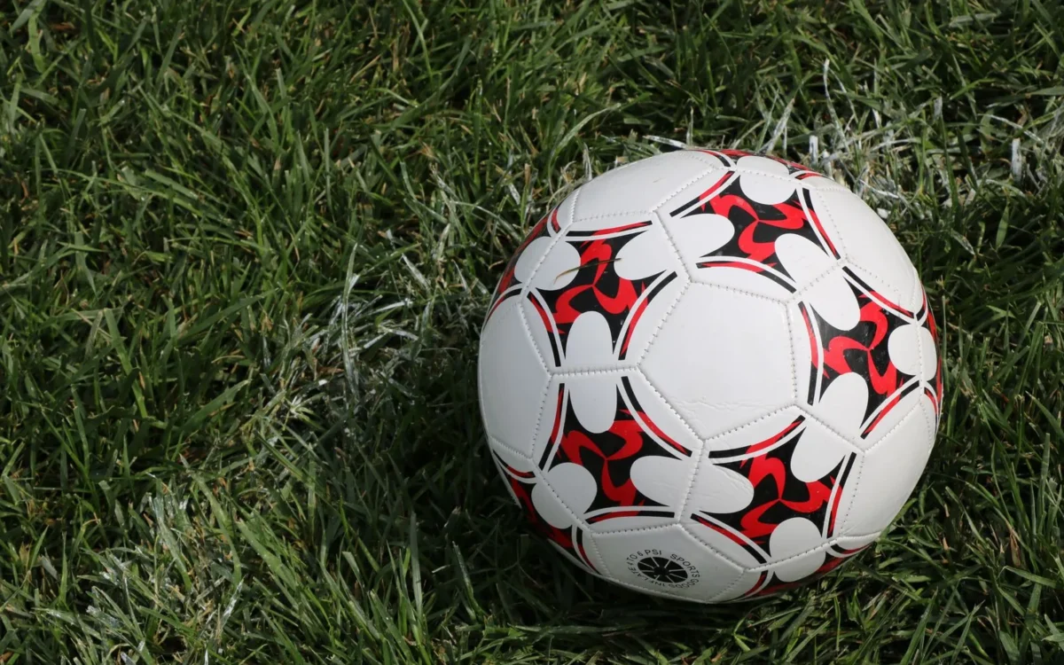 Minge de fotbal albă, cu modele roșii și negre, așezată pe iarbă