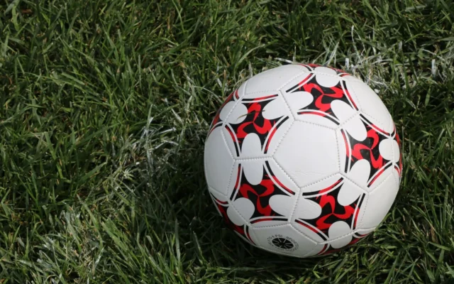 Minge de fotbal albă, cu modele roșii și negre, așezată pe iarbă