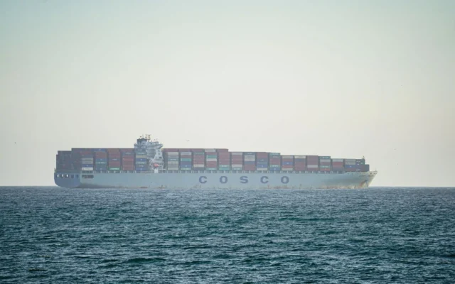 Navă portcontainer cu cocă gri și containere colorate pe punte, pe mare