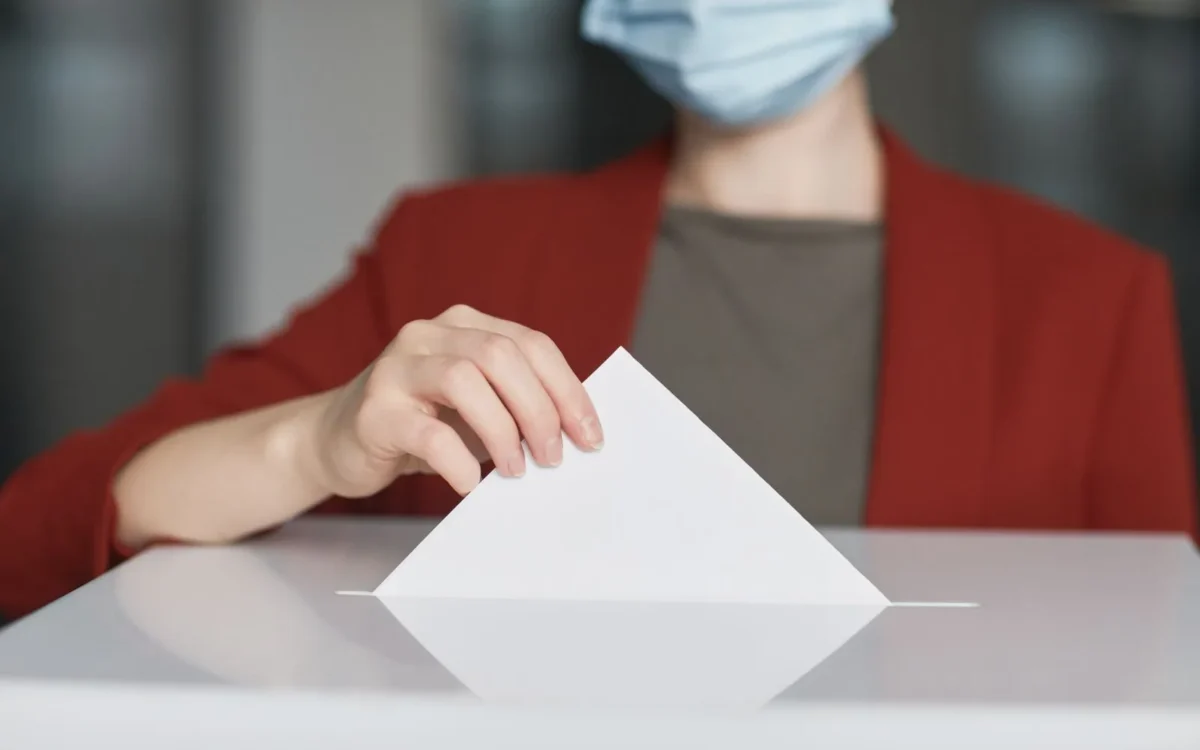 Persoană cu mască introduce un buletin de vot într-o urnă