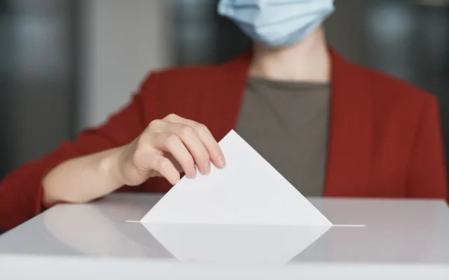Persoană cu mască introduce un buletin de vot într-o urnă