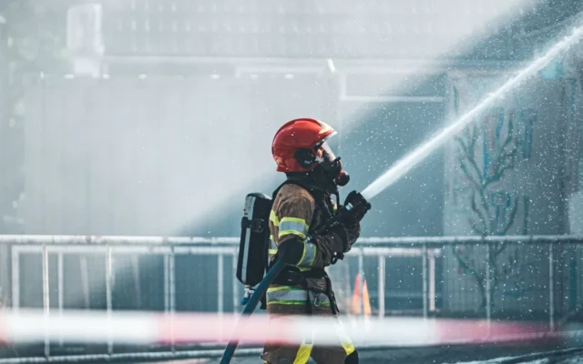 Pompier cu cască roșie și aparat de respirat, proiectând apă cu un furtun