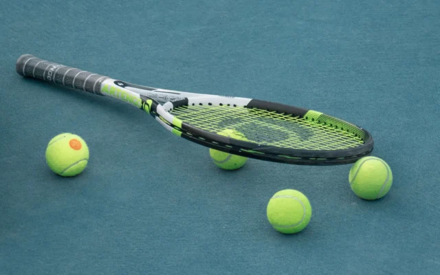 Rachetă de tenis și patru mingi galbene pe un teren albastru